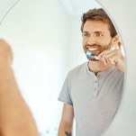 Man brushing his teeth in front of bathroom mirror