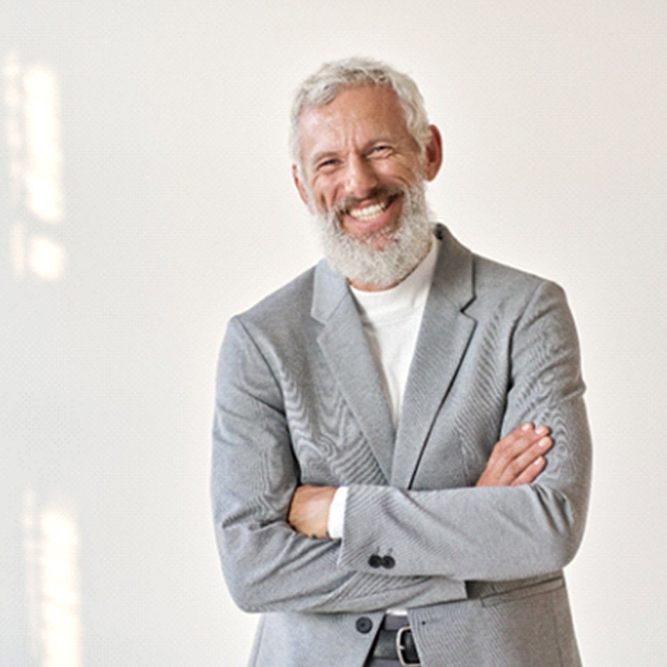 Senior man in grey suit smiling with arms folded