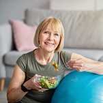 older woman eating salad on exercise ball