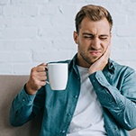 A young man holding a coffee mug and feeling an ache in his mouth