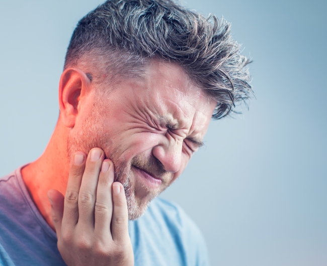 Man in need of emergency dentistry holding cheek in pain