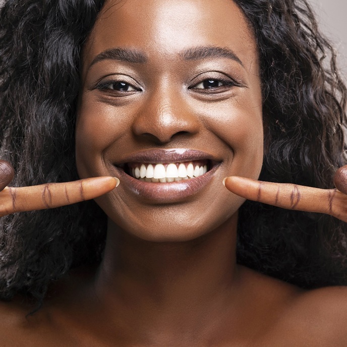 A young woman pointing to her brighter smile after undergoing teeth whitening in St. Johns