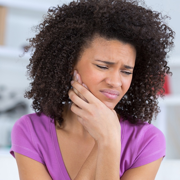Woman in need of wisdom tooth extraction holding cheek in pain